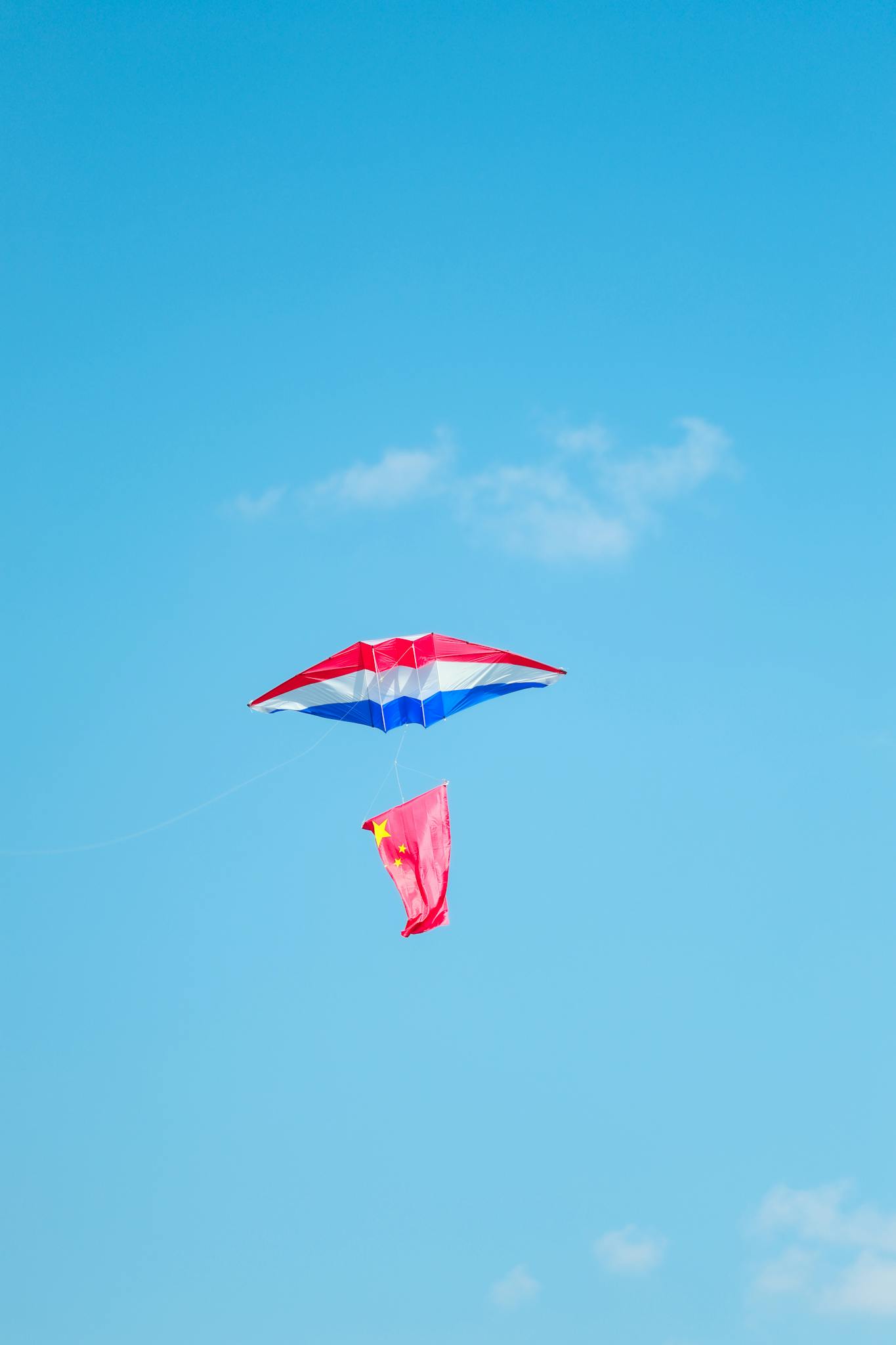 Bright red, white, and blue kite soaring high against a clear blue sky, symbolizing freedom.