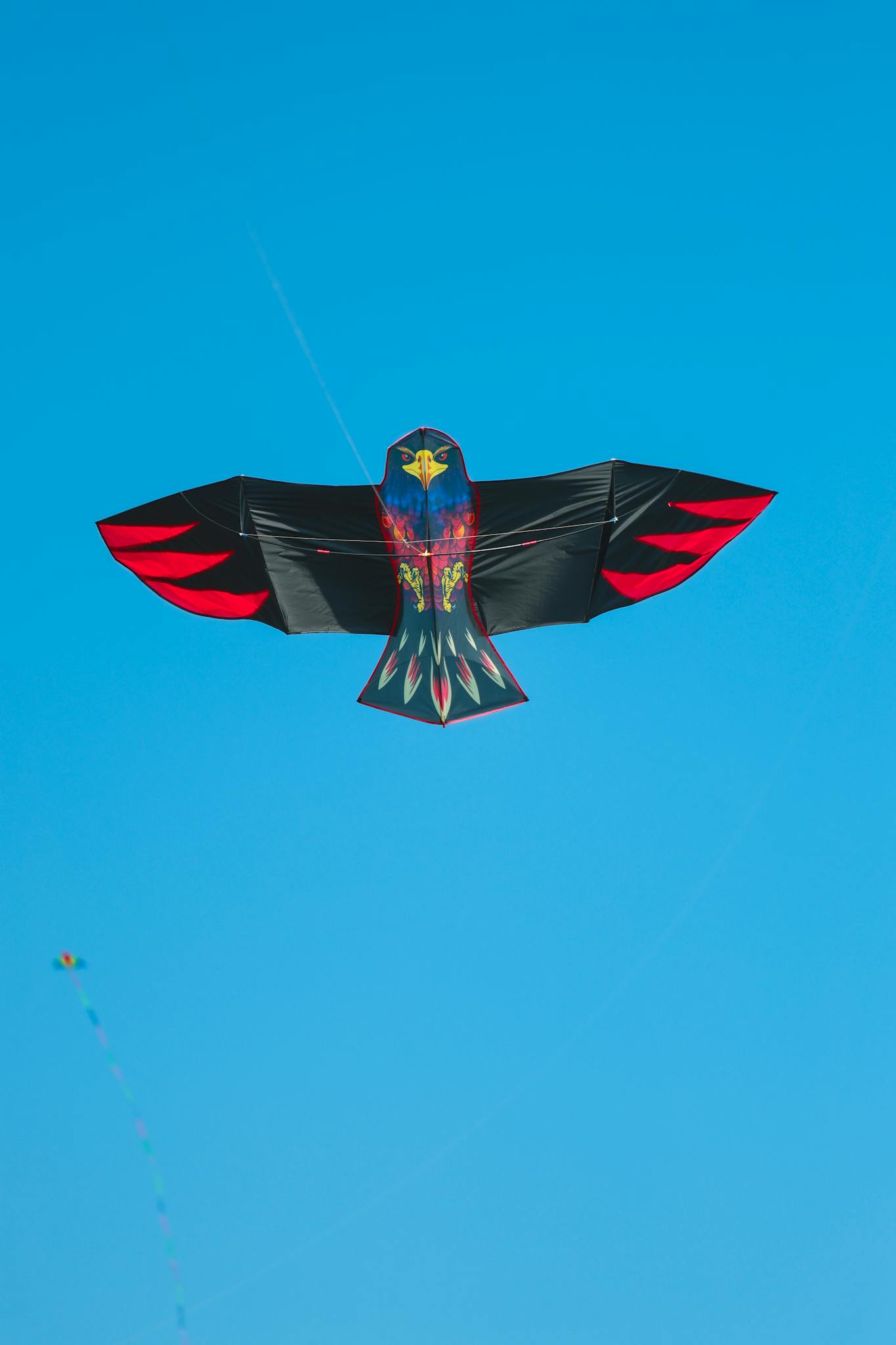 Vivid bird-shaped kite with red accents flying high in a vibrant blue sky.